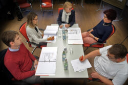 Flexibilität oder klare Regeln? Sitzungssimulator Gruppe Sitzungsleiterin Tisch ernst skeptisch