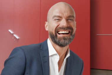 Seminare Führung Management Mann Anzug lachen Blick Büro rot / Grafik: TELOS - 2812bw