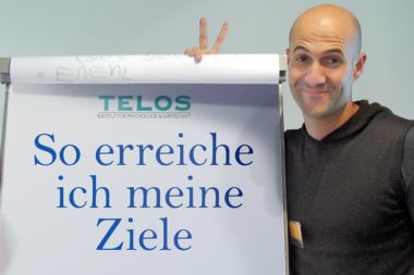 Mann Siegeszeichen lächelnd am Flipchart So erreiche ich meine Ziele / Foto: TELOS - 07244dg